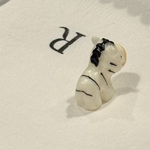 Pico-Frank, a tiny ceramic zebra, sitting in a luxury hotel gift box on white tissue paper